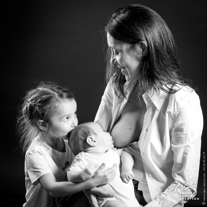 Joli portrait studio d'une mère allaitant son bébé pendant que la grande sœur lui fait un bisous